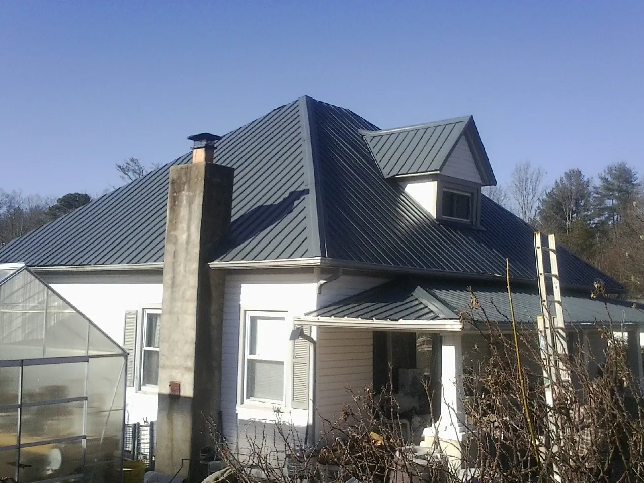 Dark blue standing seam metal roof on a white farmhouse with dormer — Slate & Tile Roof Repair by Roofing Brothers in Fair Lawn