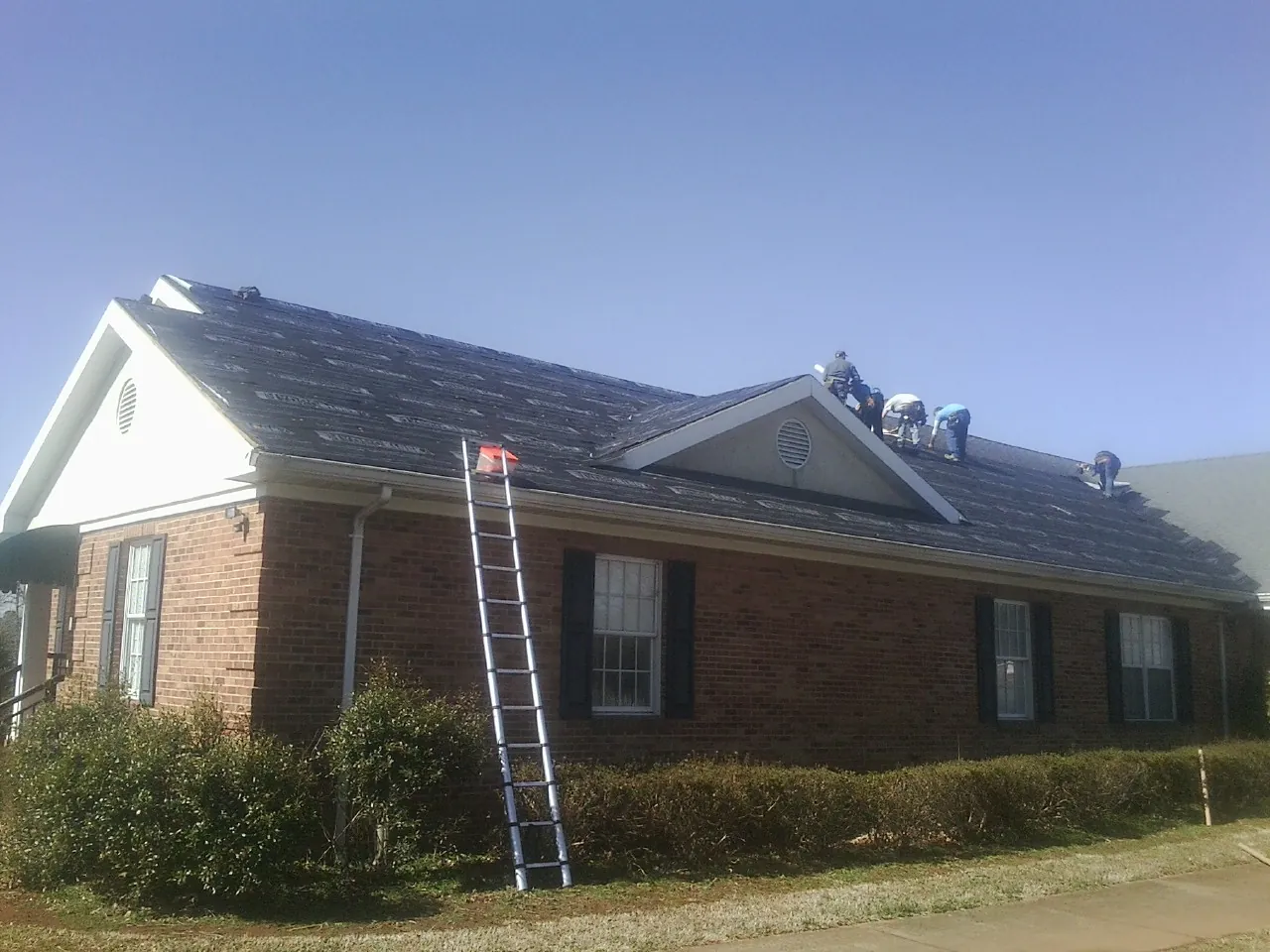 Crew tearing shingles off a brick ranch roof with a ladder set — Emergency Roof Repair work by our crew in Fair Lawn
