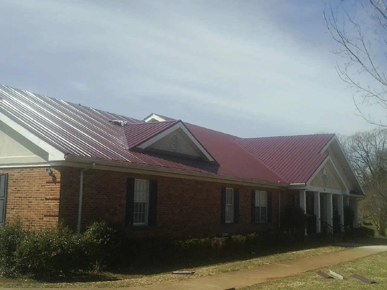 Red metal roof with gabled entries on a long brick building, from a Hail Damage Roof Repair job in Fair Lawn