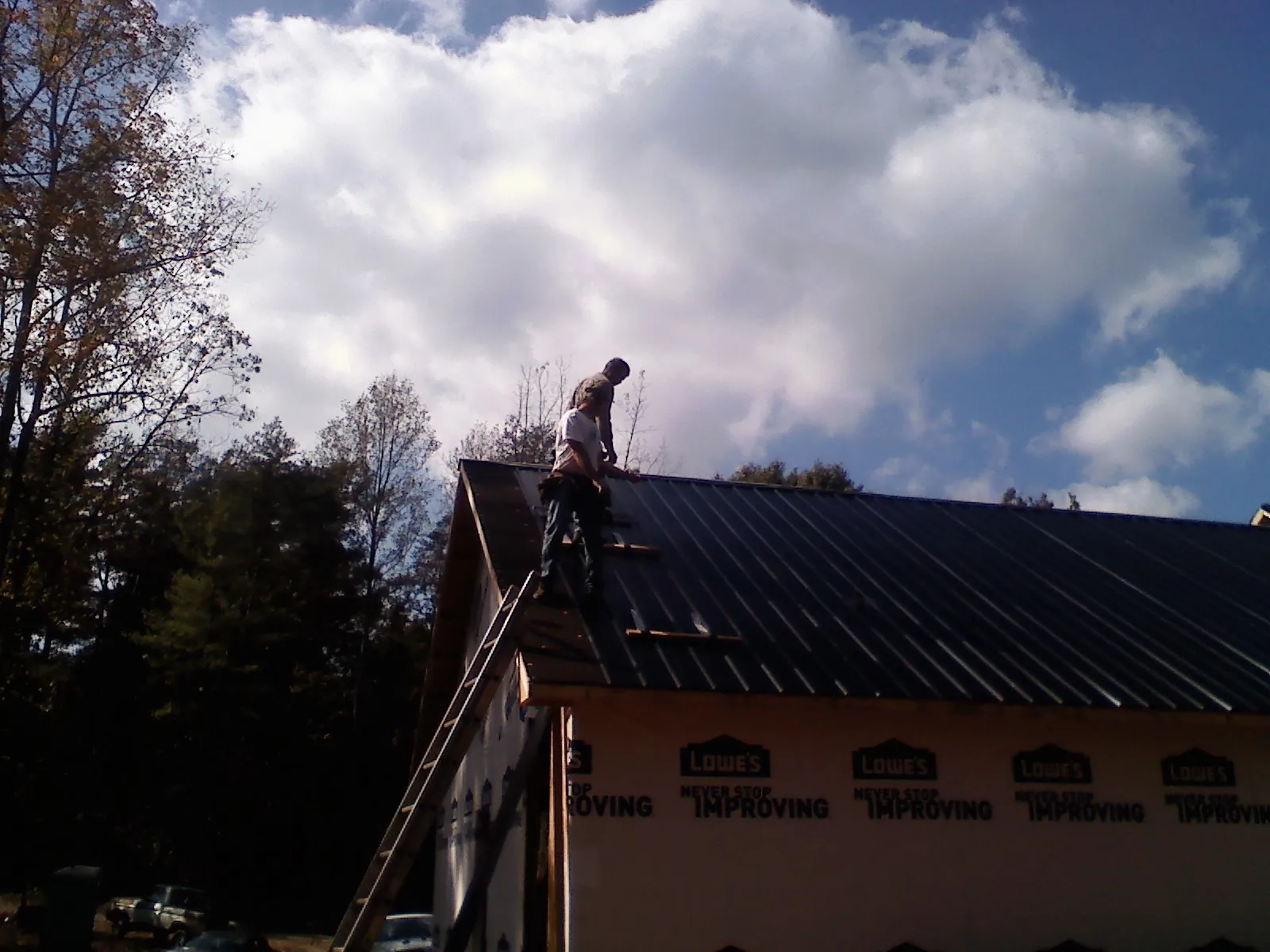 Roofer fastening dark metal panels high against a cloudy sky, from a Roof Inspection job in Fair Lawn