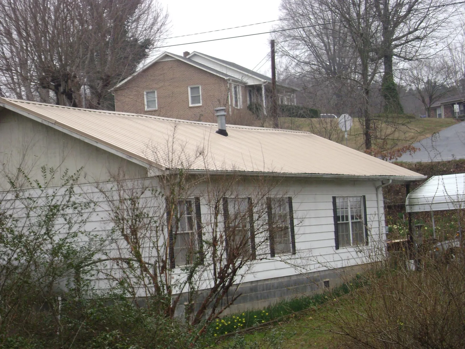 Tan metal roof on a white sided house set into a hillside — Commercial Roofing by Roofing Brothers in Fair Lawn